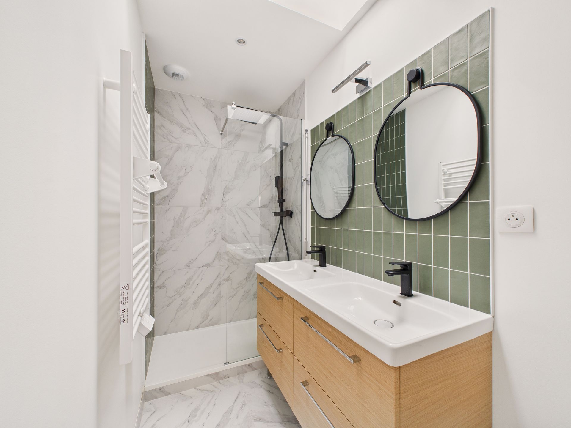Meuble double vasque en bois sous deux miroirs ronds, devant un mur carrelé vert.