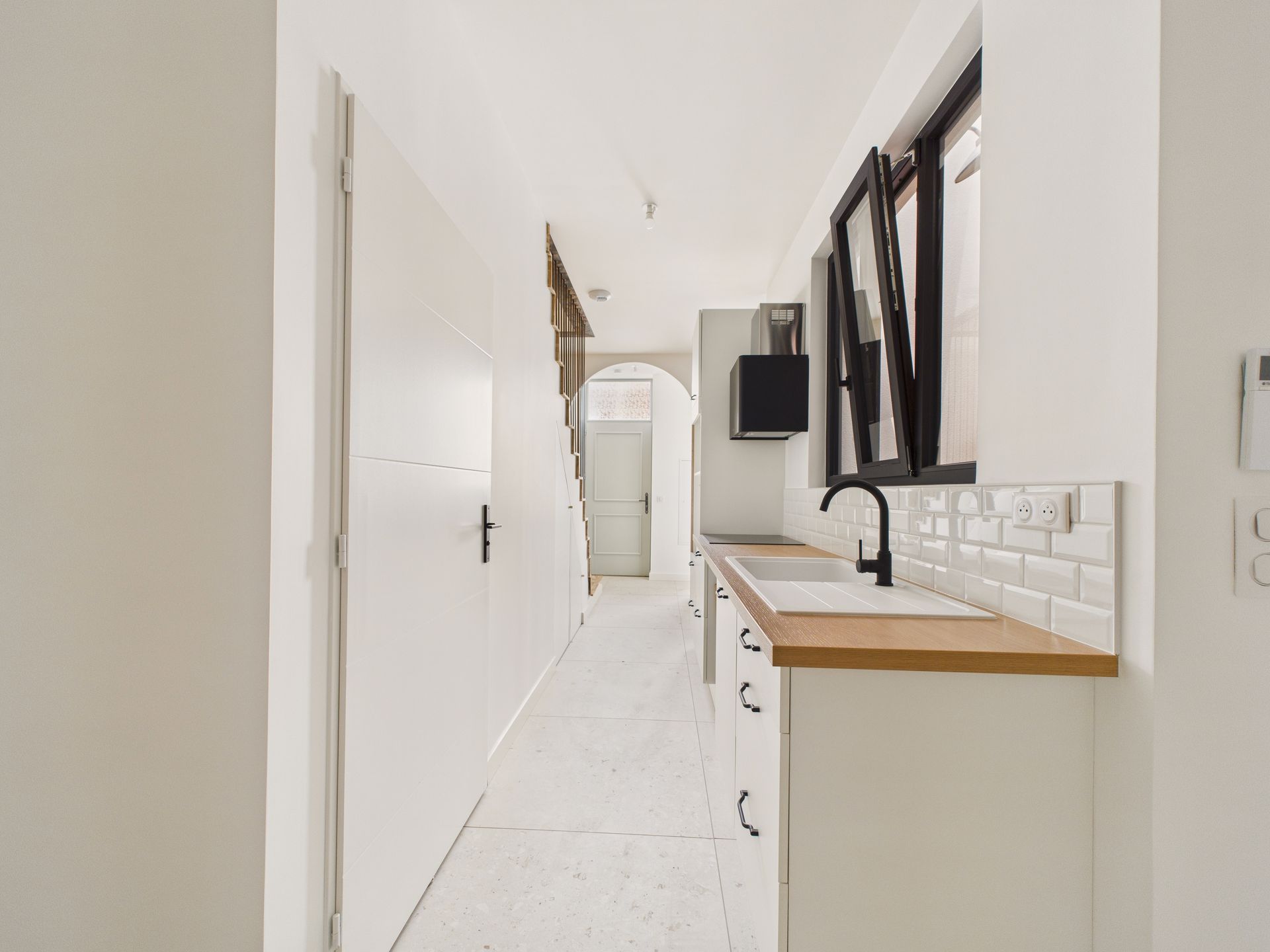 Cuisine étroite blanche avec des fenêtres noires et un plan de travail en bois.
