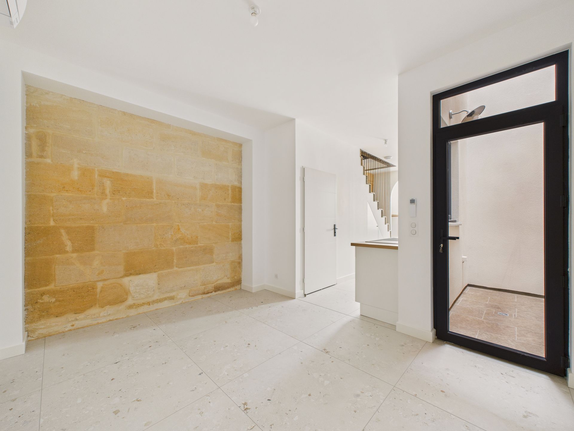 Entrée avec une porte vitrée noire et un mur intérieur en pierre apparente.