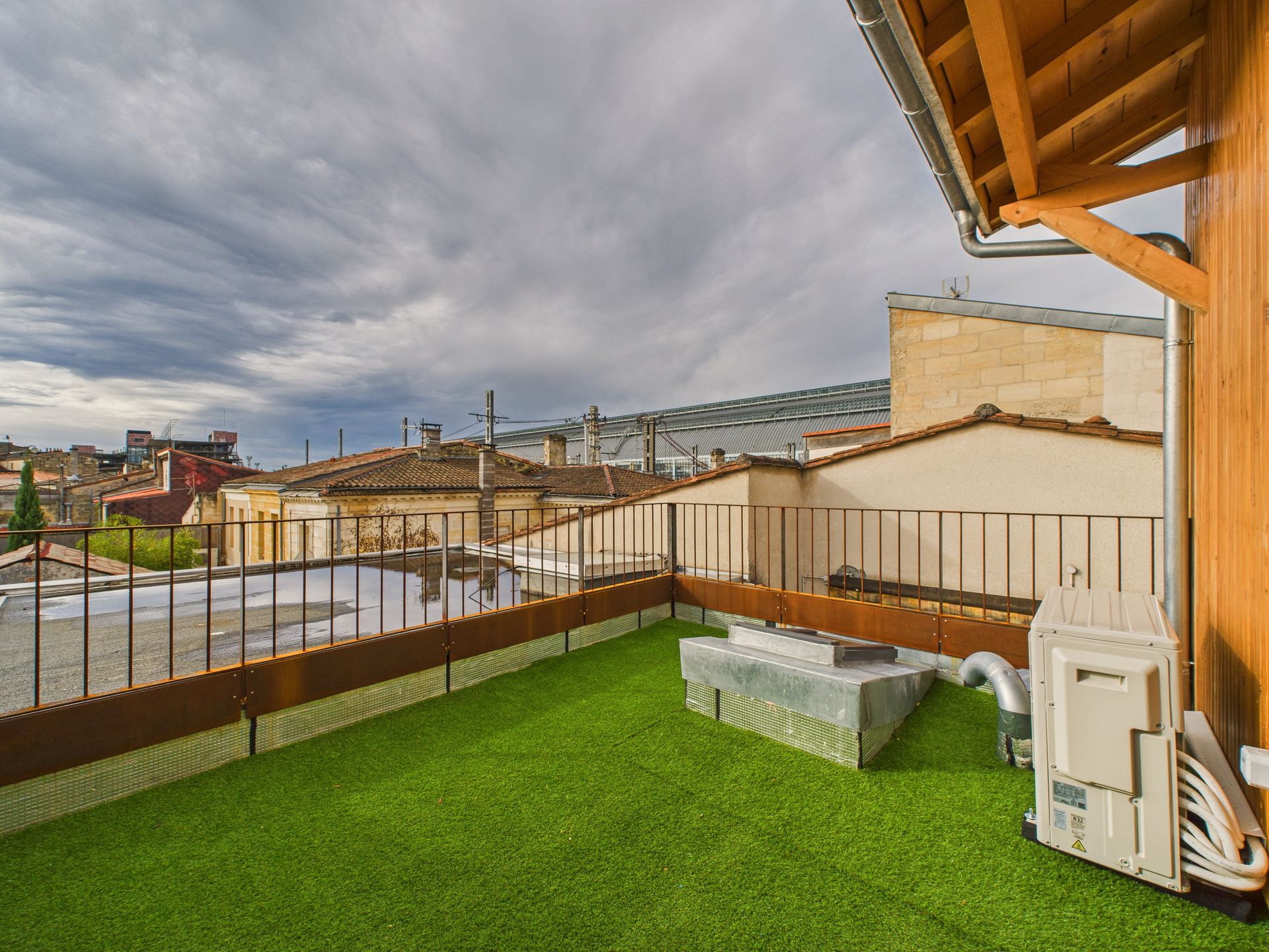 Petite terrasse avec un sol vert et un garde-corps donnant sur les toits.