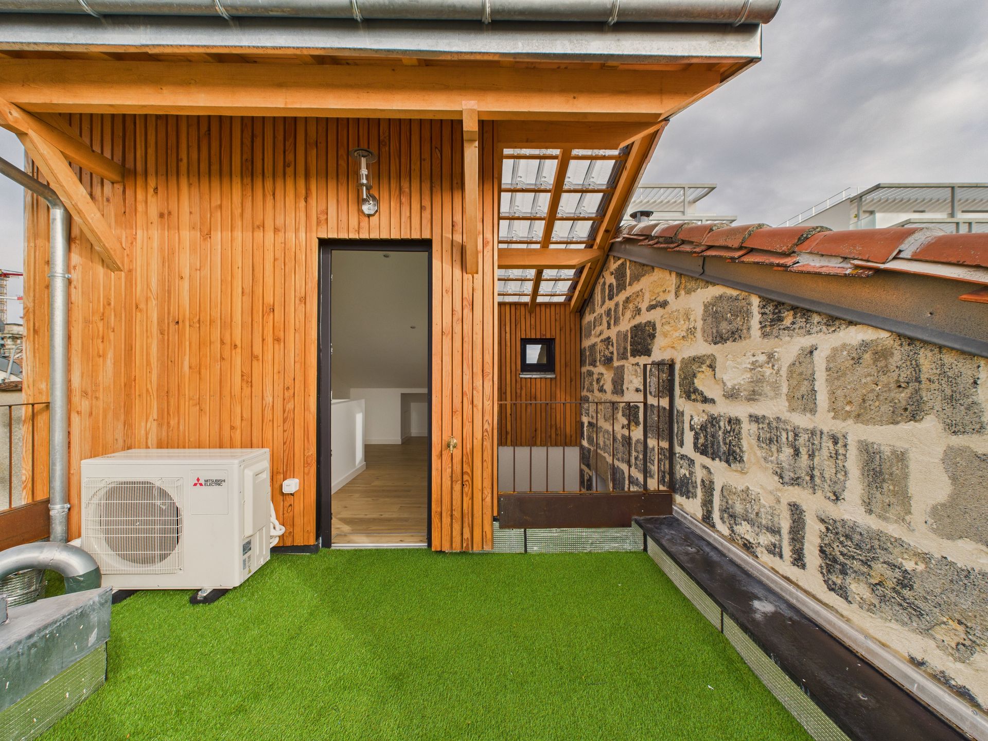 Façade de terrasse en bardage bois, avec une unité extérieure de climatisation.