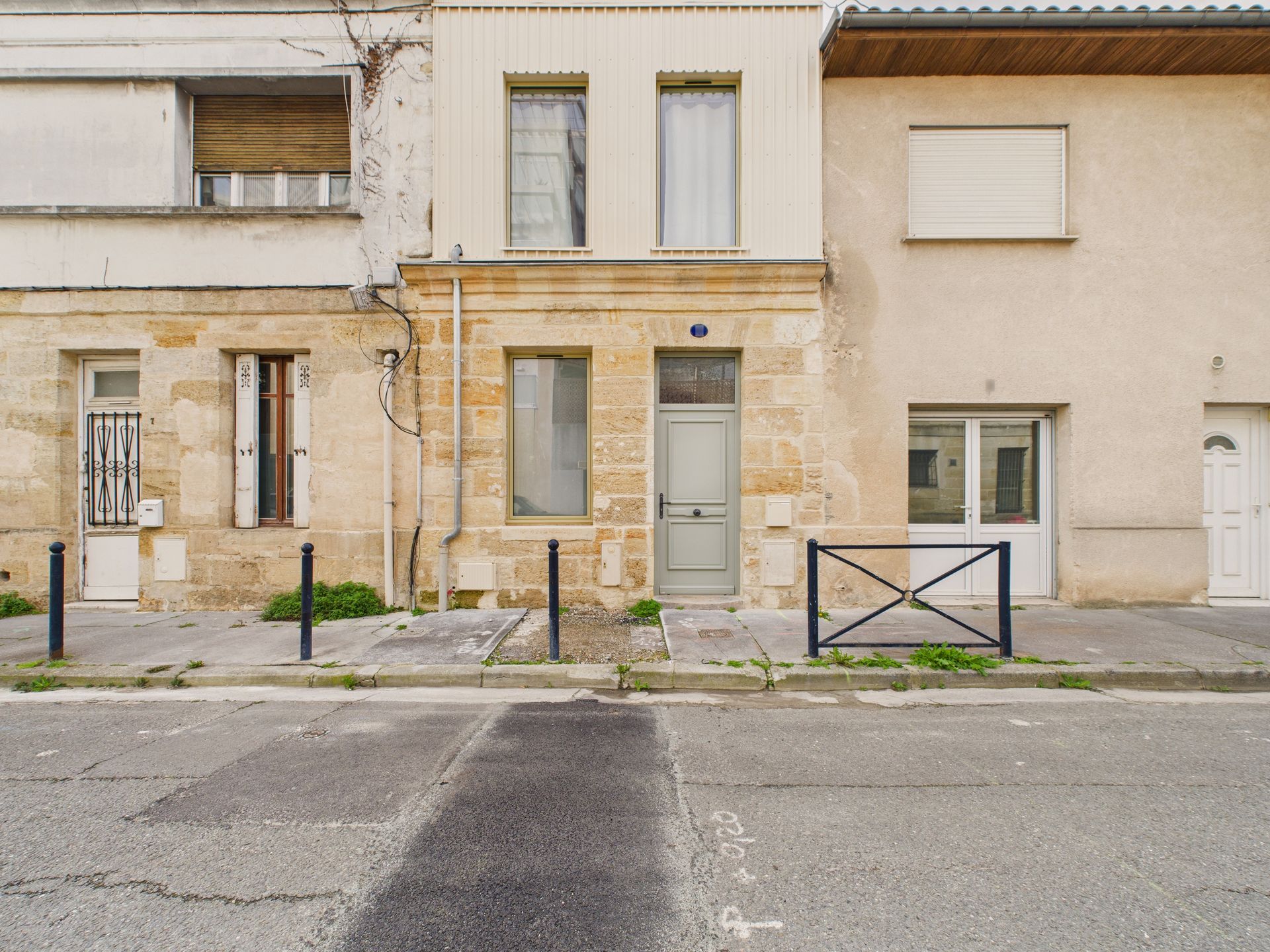 Façade sur rue d’une maison en pierre entre deux bâtiments voisins.