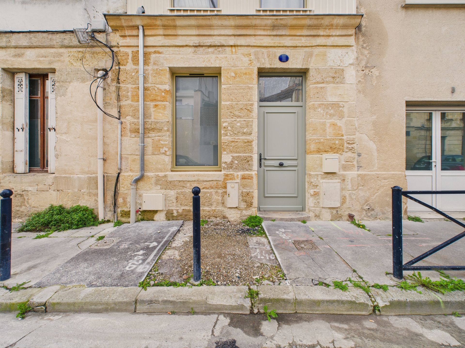 Entrée d’une maison en pierre avec une porte et une fenêtre grises.