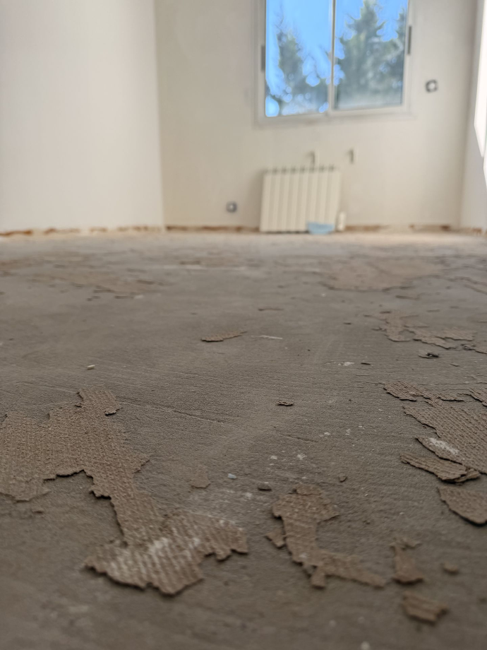 Sol brut présentant des résidus de revêtement dans une pièce vide.