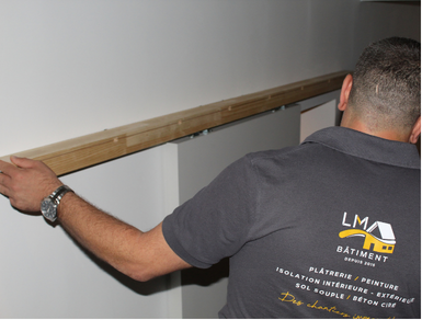 Artisan mesurant une ossature contre un mur.