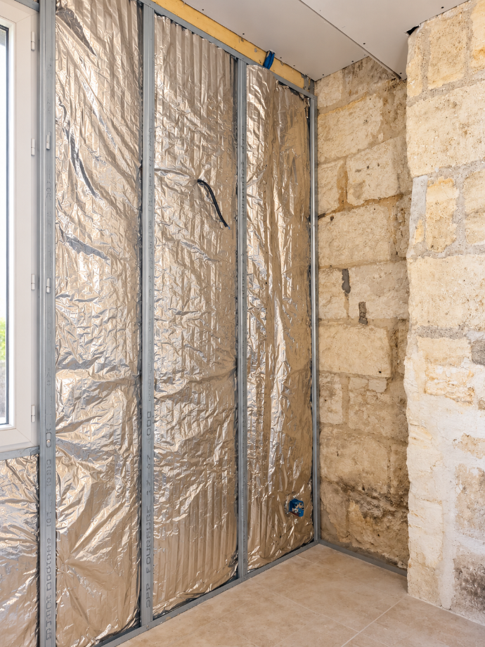 Isolant posé entre des montants métalliques contre un mur en pierre.