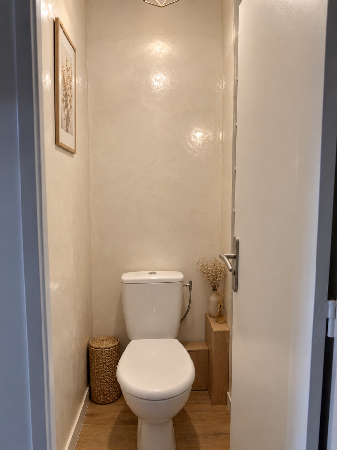 Toilettes avec des murs beiges à effet de matière et des spots au plafond.
