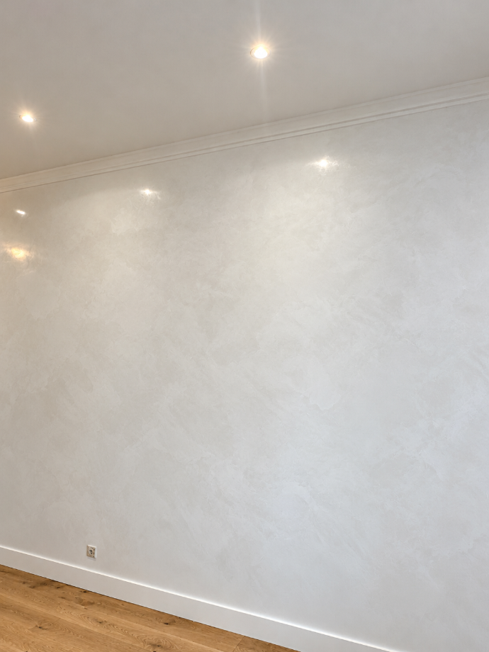 Mur clair à effet nuancé, éclairé par des spots de plafond.