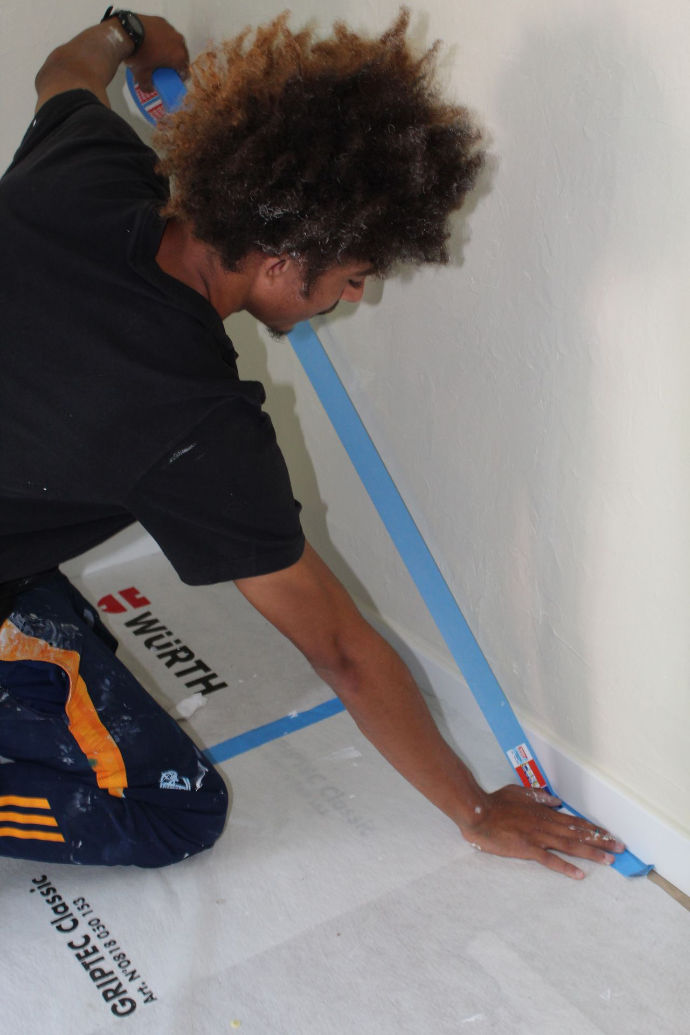 Artisan protégeant la jonction d’un mur et du sol avec du ruban de masquage.