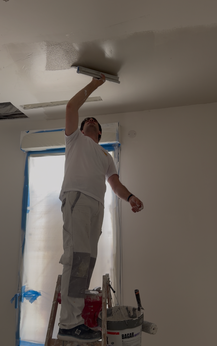 Artisan travaillant au rouleau sur un plafond blanc.