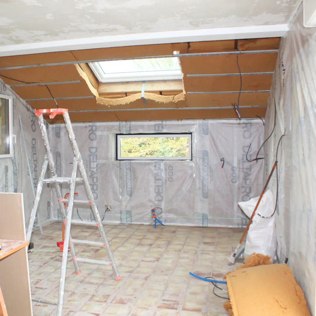 Pièce sous toiture en travaux, avec une membrane sur les murs et un escabeau.