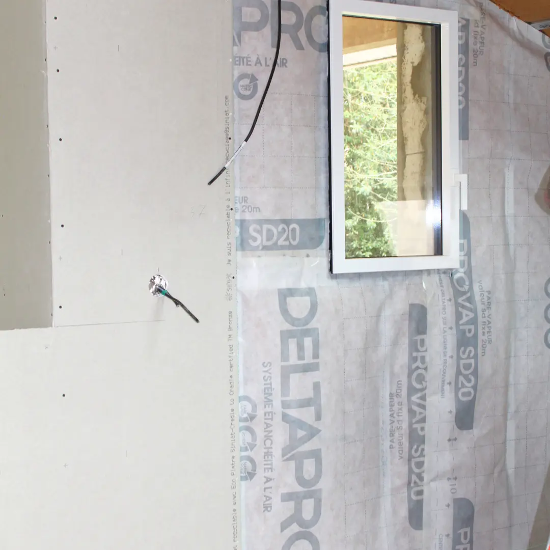 Mur partiellement fermé par des plaques de plâtre autour d’une fenêtre.