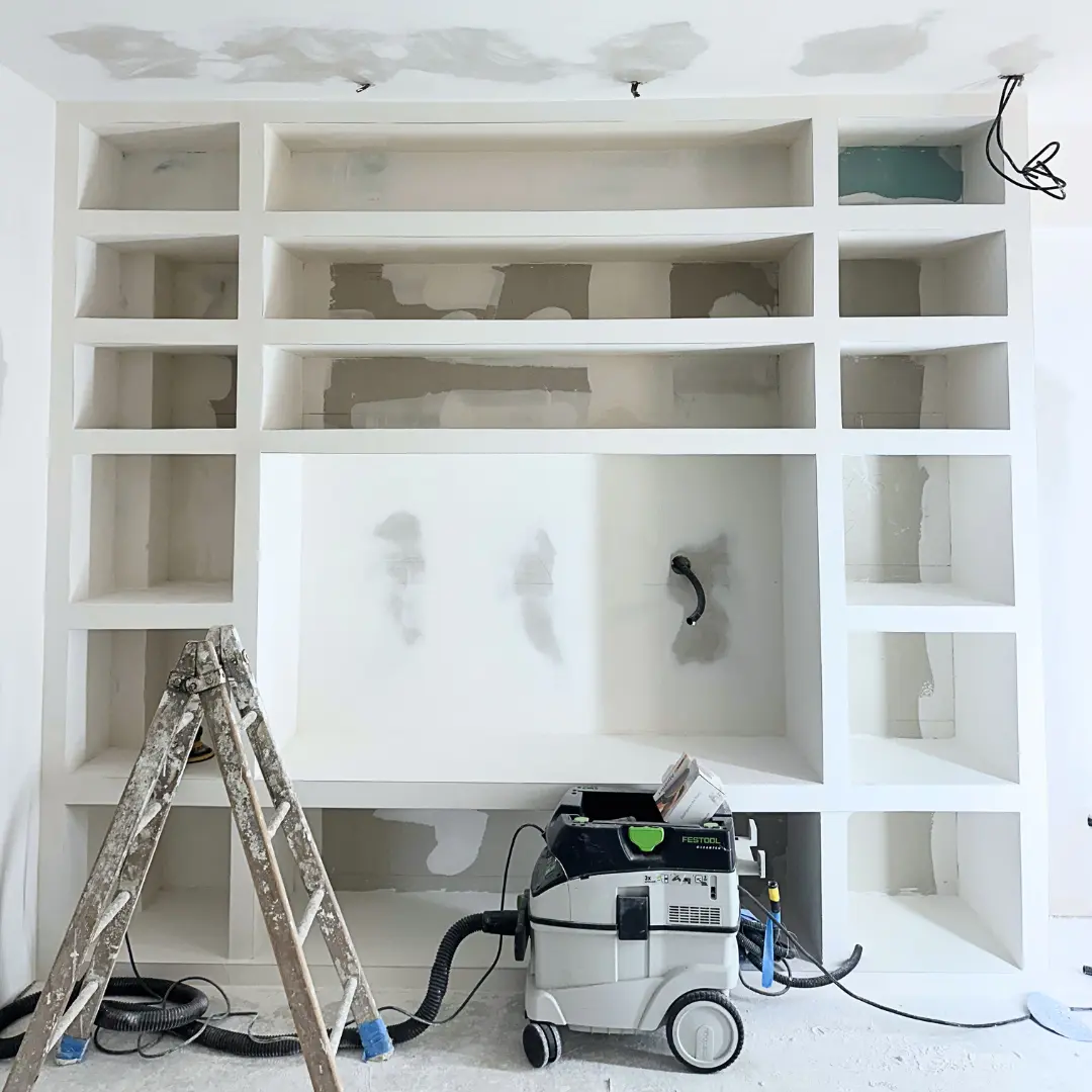 Bibliothèque intégrée avant peinture, avec un escabeau et du matériel de chantier.