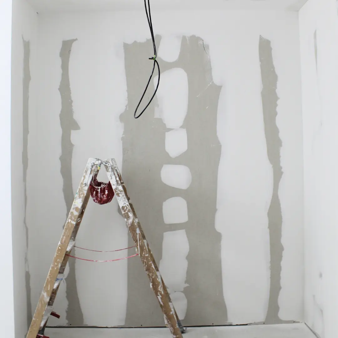 Mur en plaques de plâtre jointoyées derrière un escabeau.