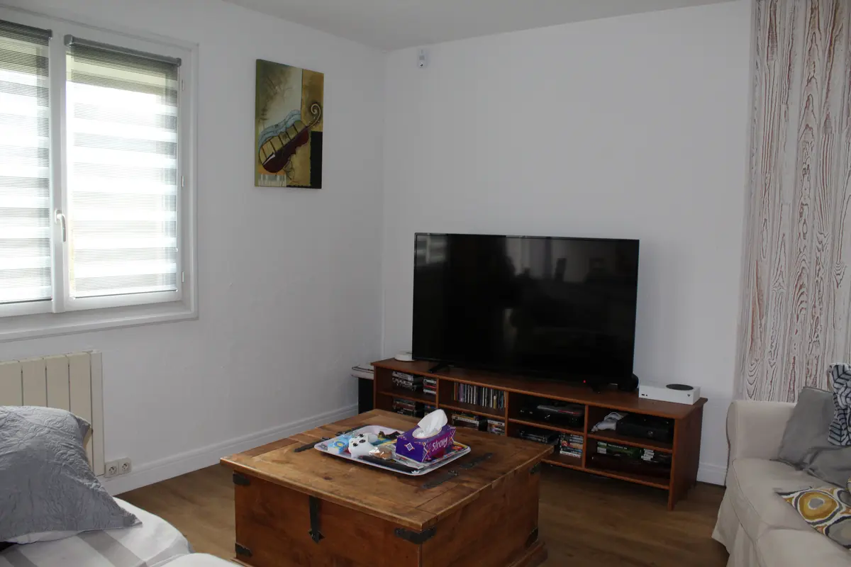 Salon meublé avec un mur clair, une télévision et un sol à effet bois.