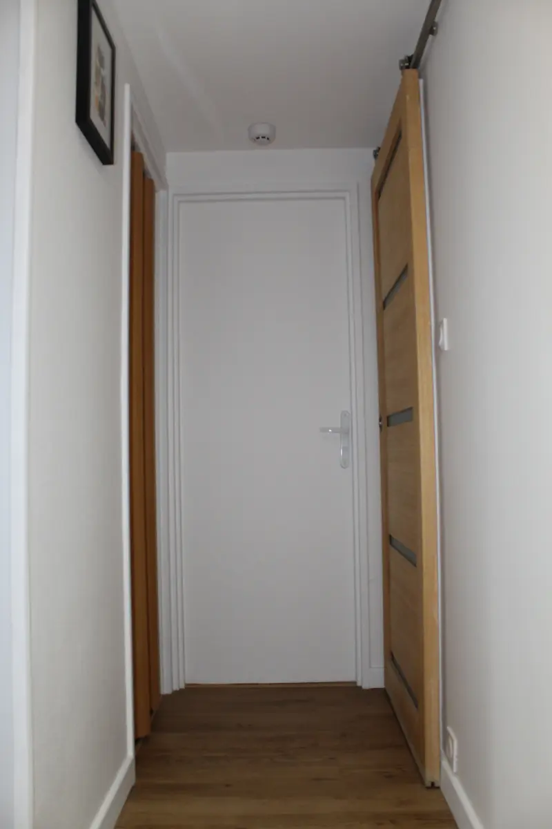 Couloir blanc et sol à effet bois entre deux portes en bois.