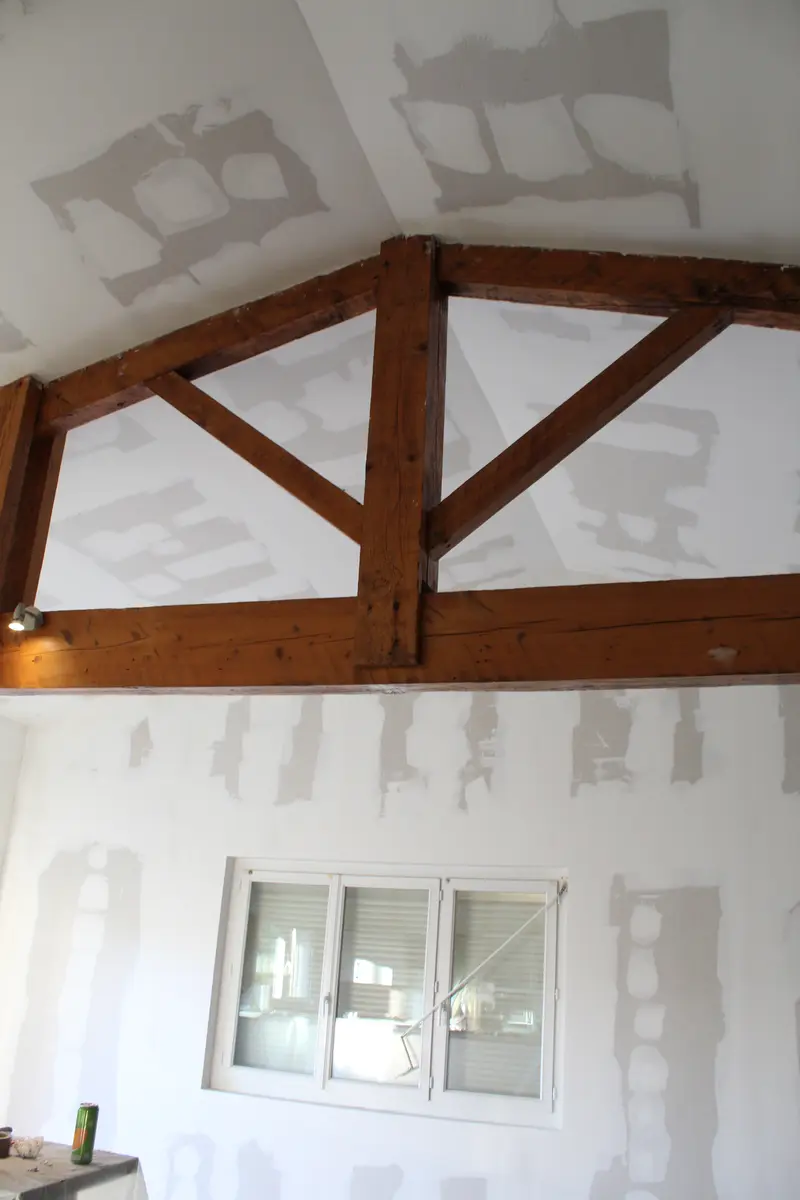 Plafond jointoyé autour d’une charpente en bois apparente.