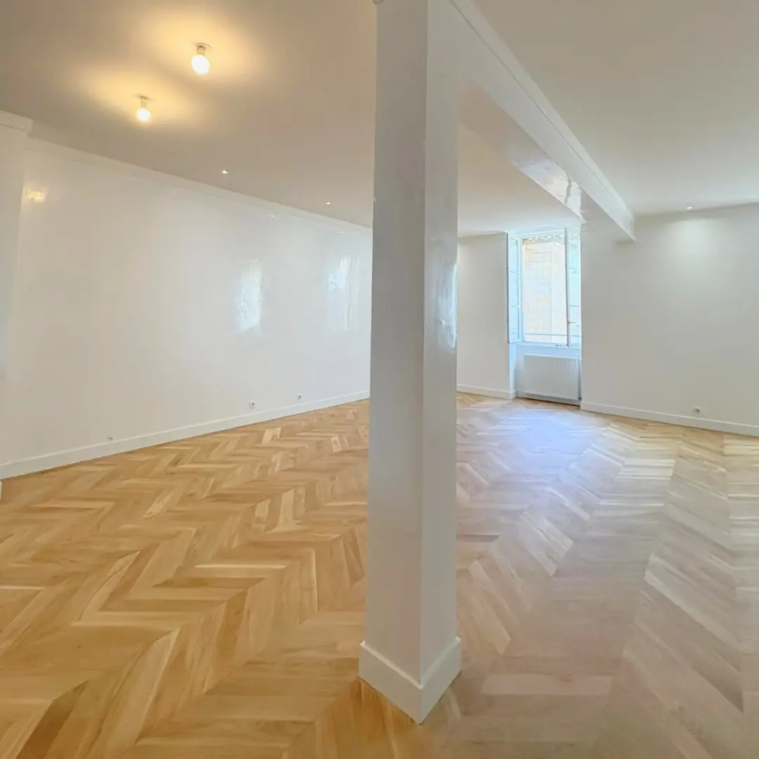 Séjour rénové avec un poteau blanc, des spots et un sol en chevrons.