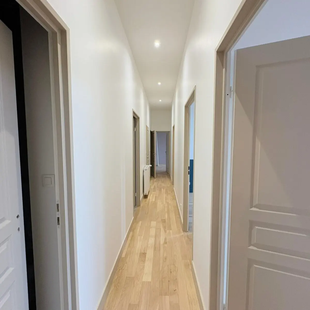 Couloir blanc avec des spots au plafond et un plancher en bois.