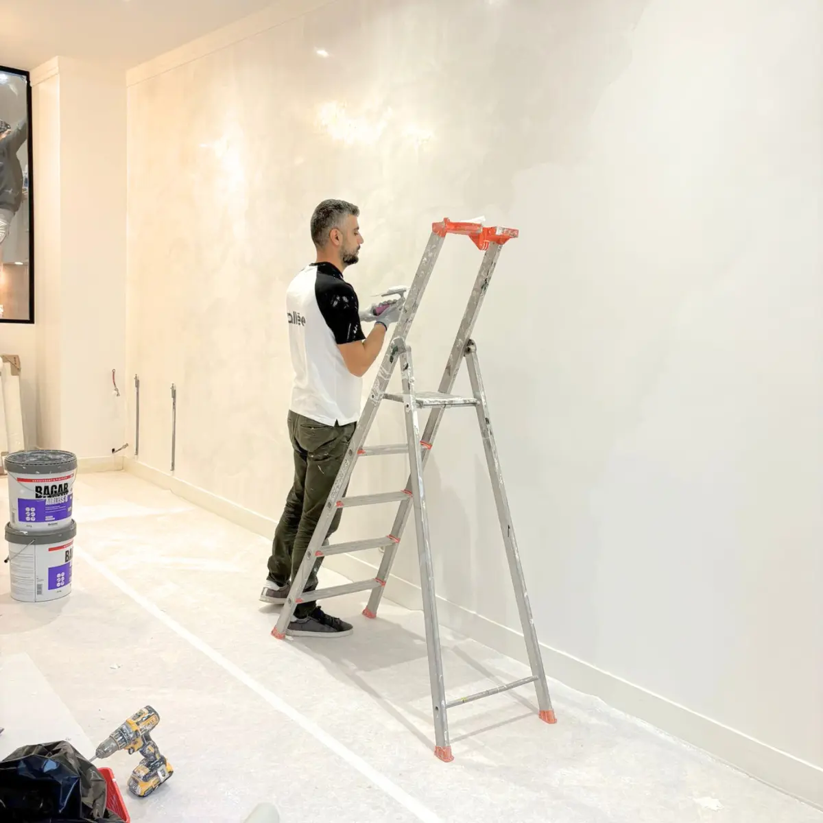 Artisan travaillant sur un mur clair à côté d’un escabeau.