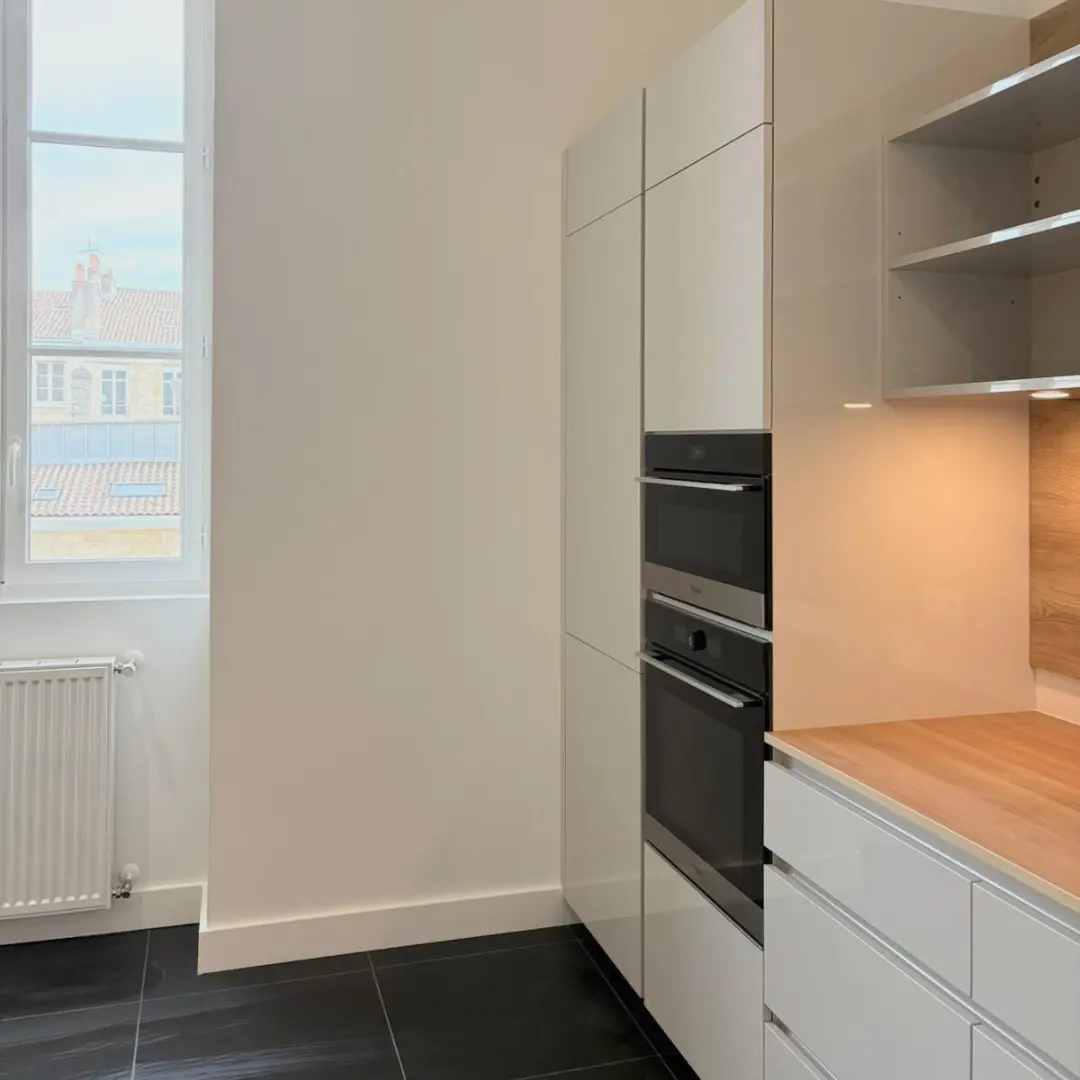 Meubles de cuisine blancs avec un four intégré et une crédence beige.