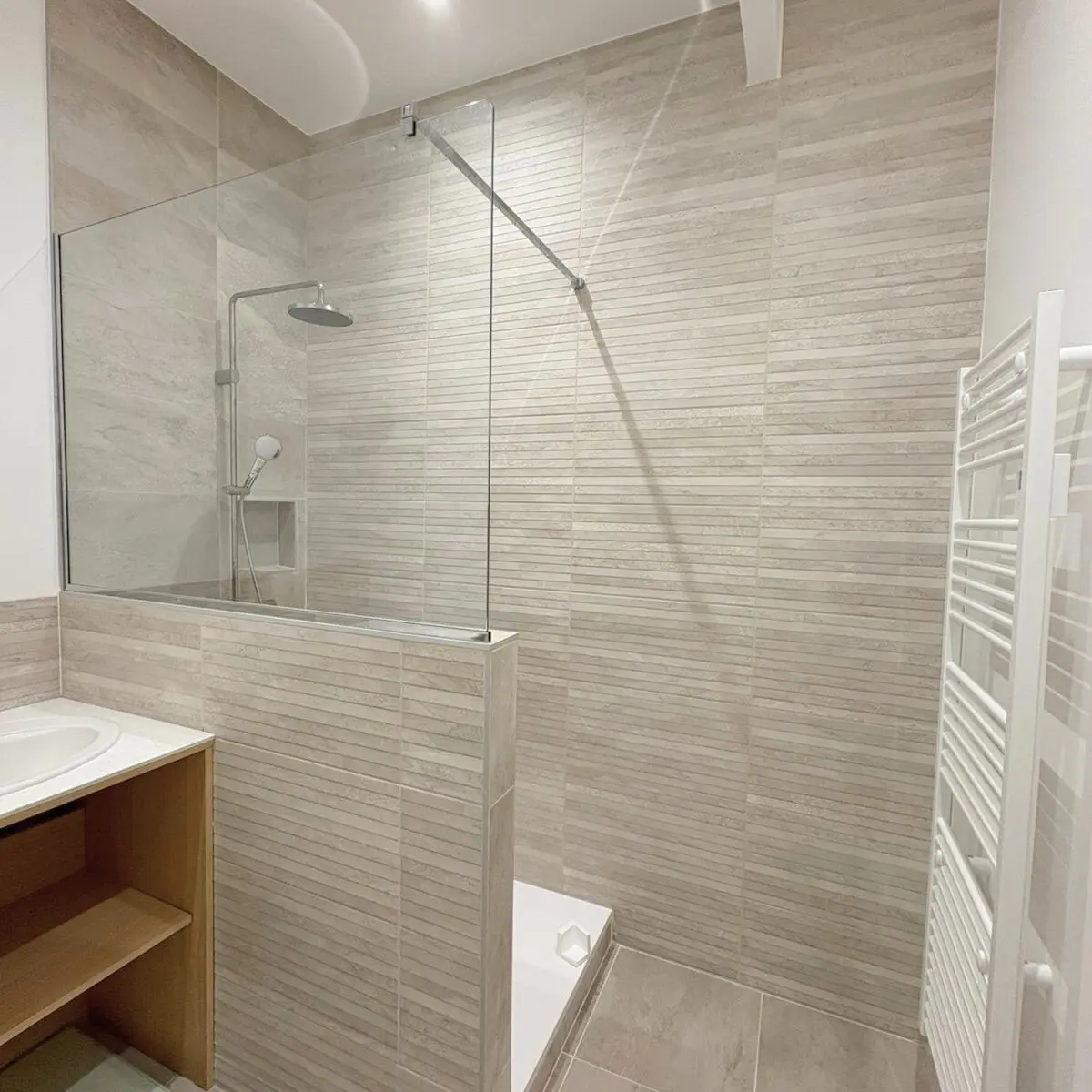 Salle de bain carrelée avec une douche vitrée et un sèche-serviettes blanc.