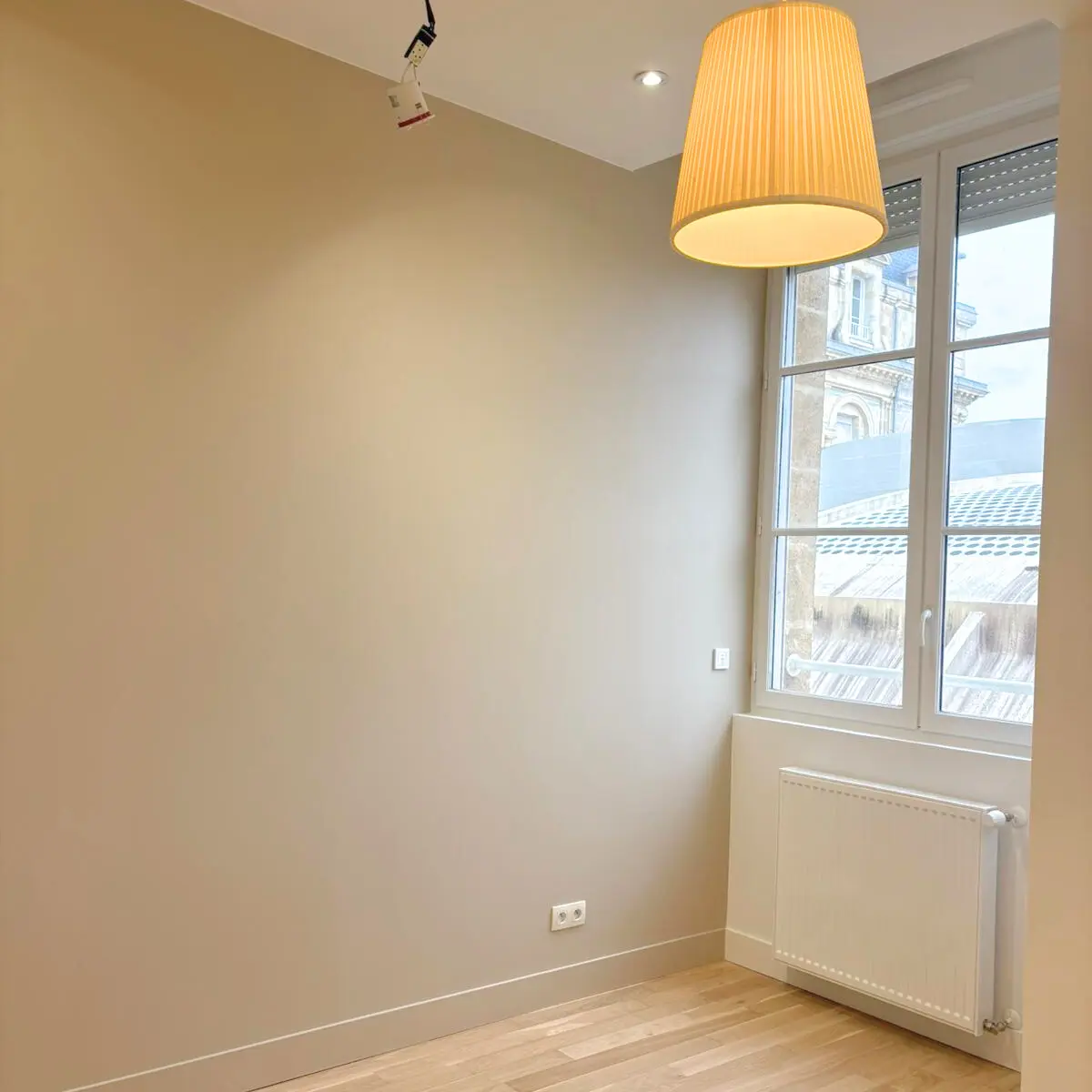 Pièce claire avec un mur de teinte beige et une suspension au plafond.