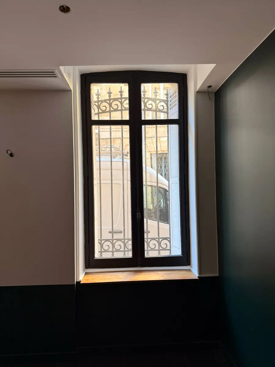 Fenêtre haute avec des encadrements contrastés entre deux murs foncés.