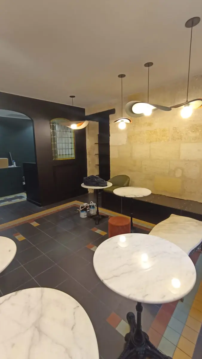 Tables rondes et suspensions dans un commerce avec un mur en pierre.