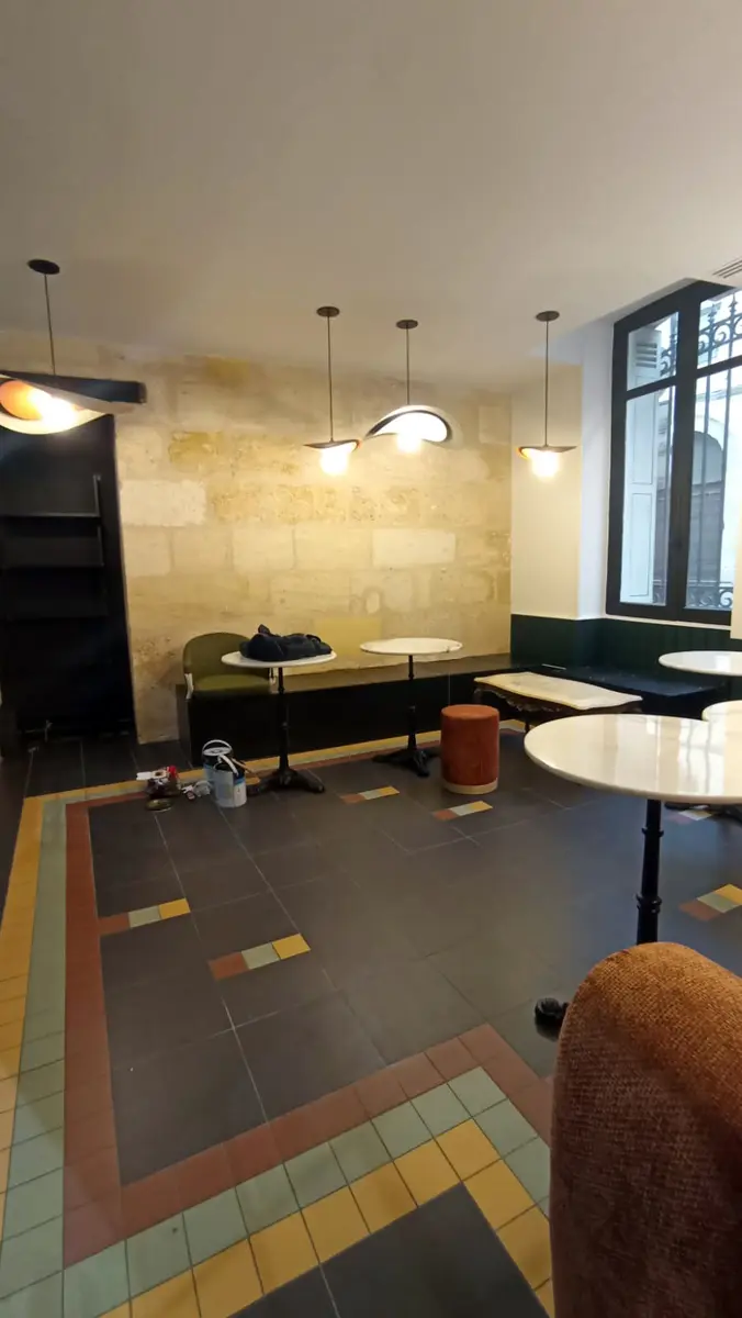 Espace de commerce avec un comptoir, des tables rondes et un mur en pierre.