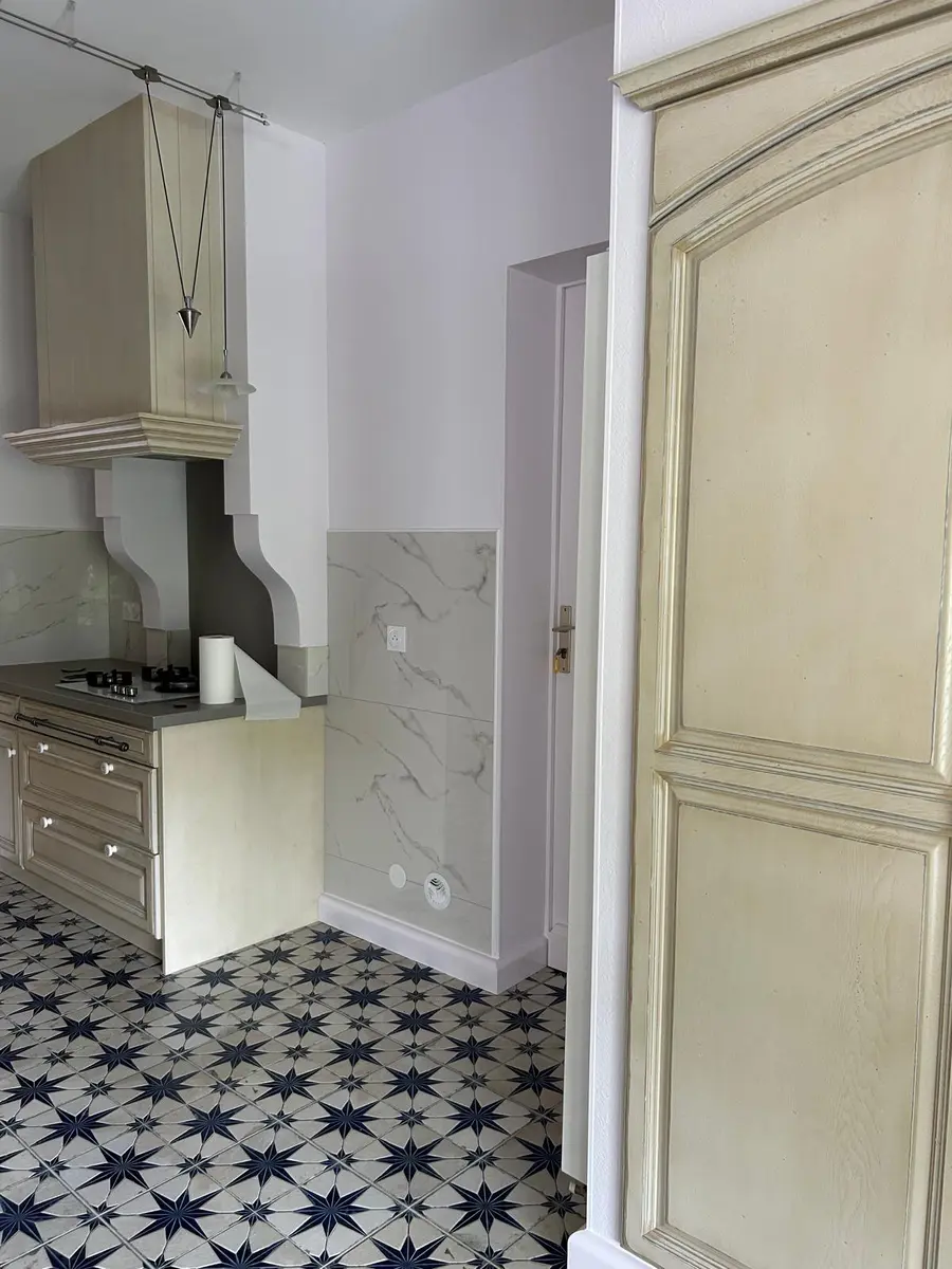 Cuisine équipée claire avec une porte à panneaux et un sol à motifs étoilés.