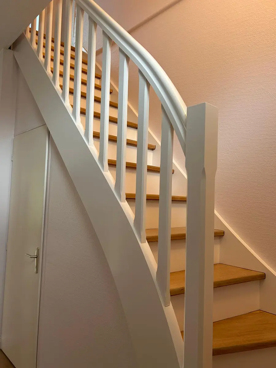 Escalier en bois avec un garde-corps et des contremarches clairs.