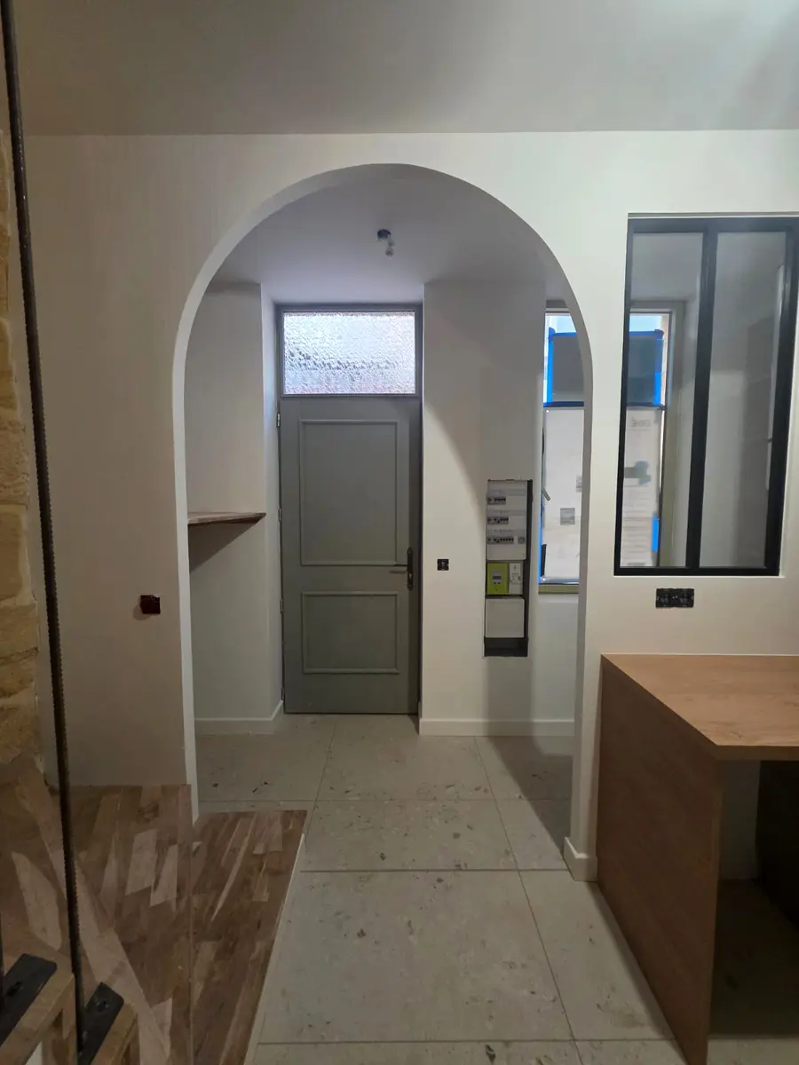 Passage cintré et verrière noire dans une entrée en rénovation.