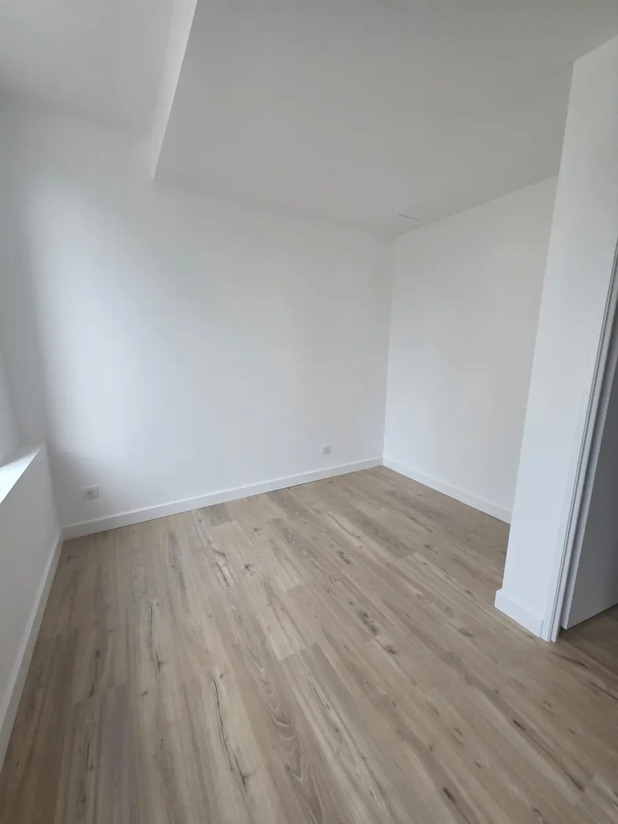 Petite pièce vide avec des murs blancs et un sol à effet bois clair.