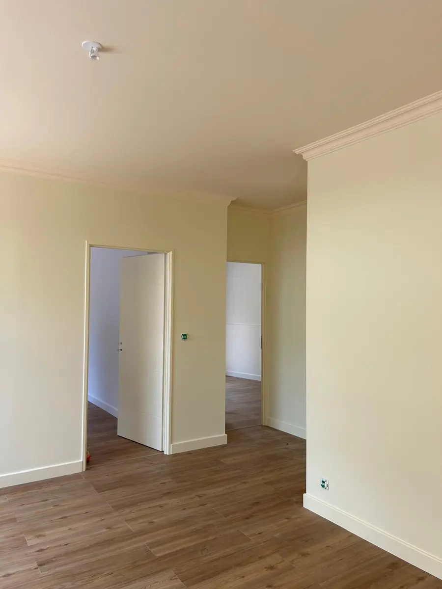 Pièce claire avec une porte blanche ouverte et un sol à effet bois.