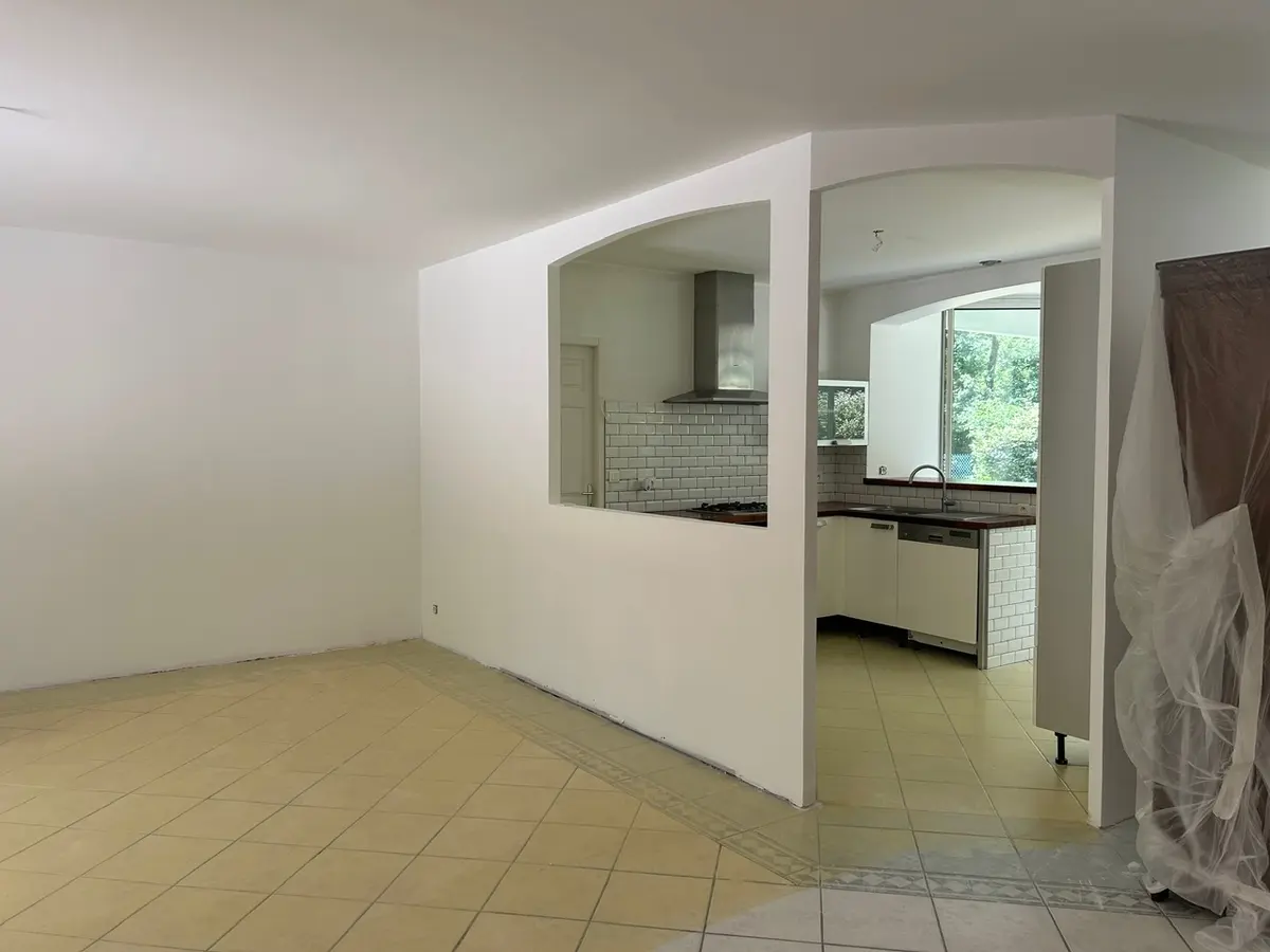 Pièce avant rénovation avec un sol carrelé et une ouverture vers la cuisine.