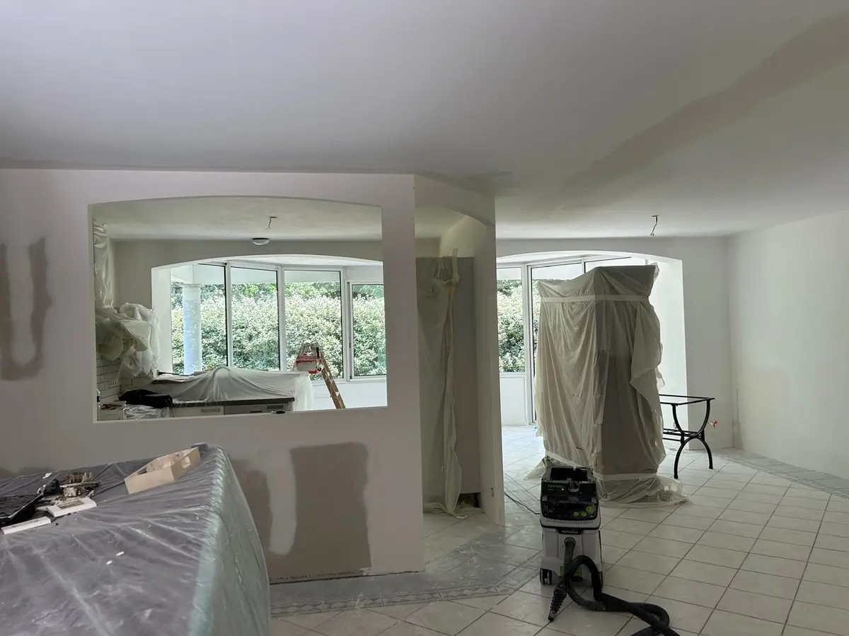 Salon en travaux avec des cloisons jointoyées et du mobilier protégé.
