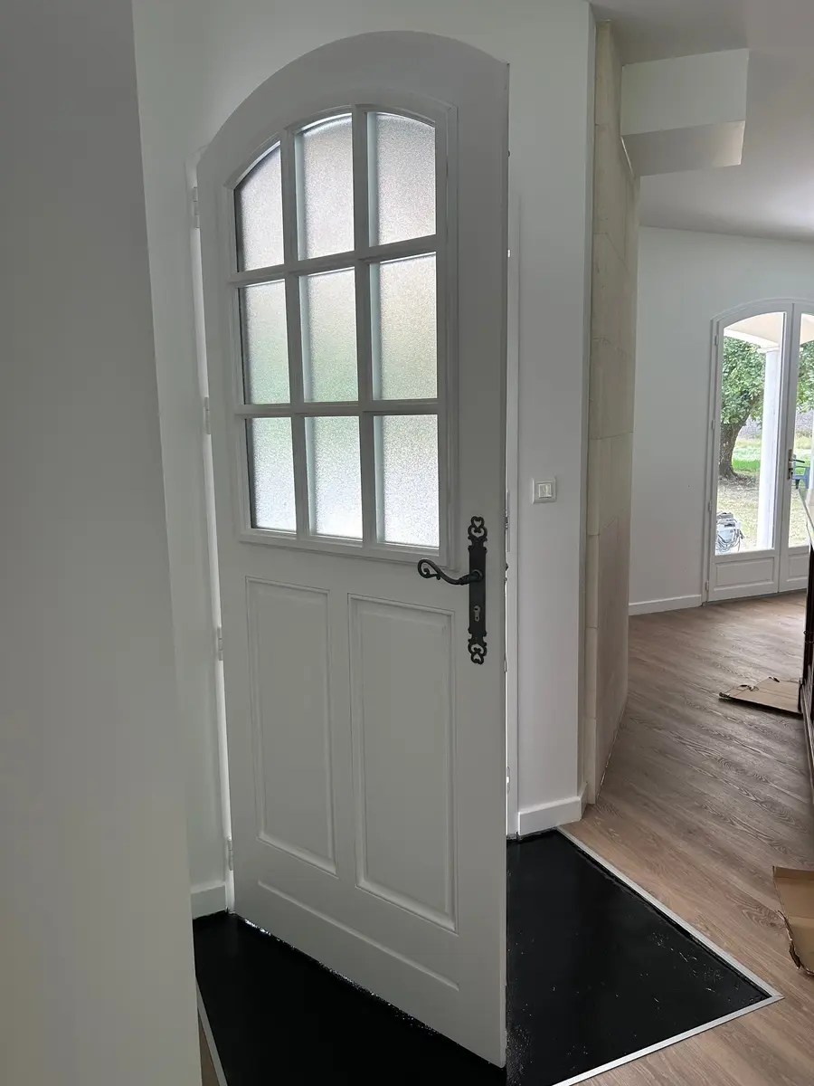 Porte d’entrée vitrée blanche donnant sur un intérieur rénové.