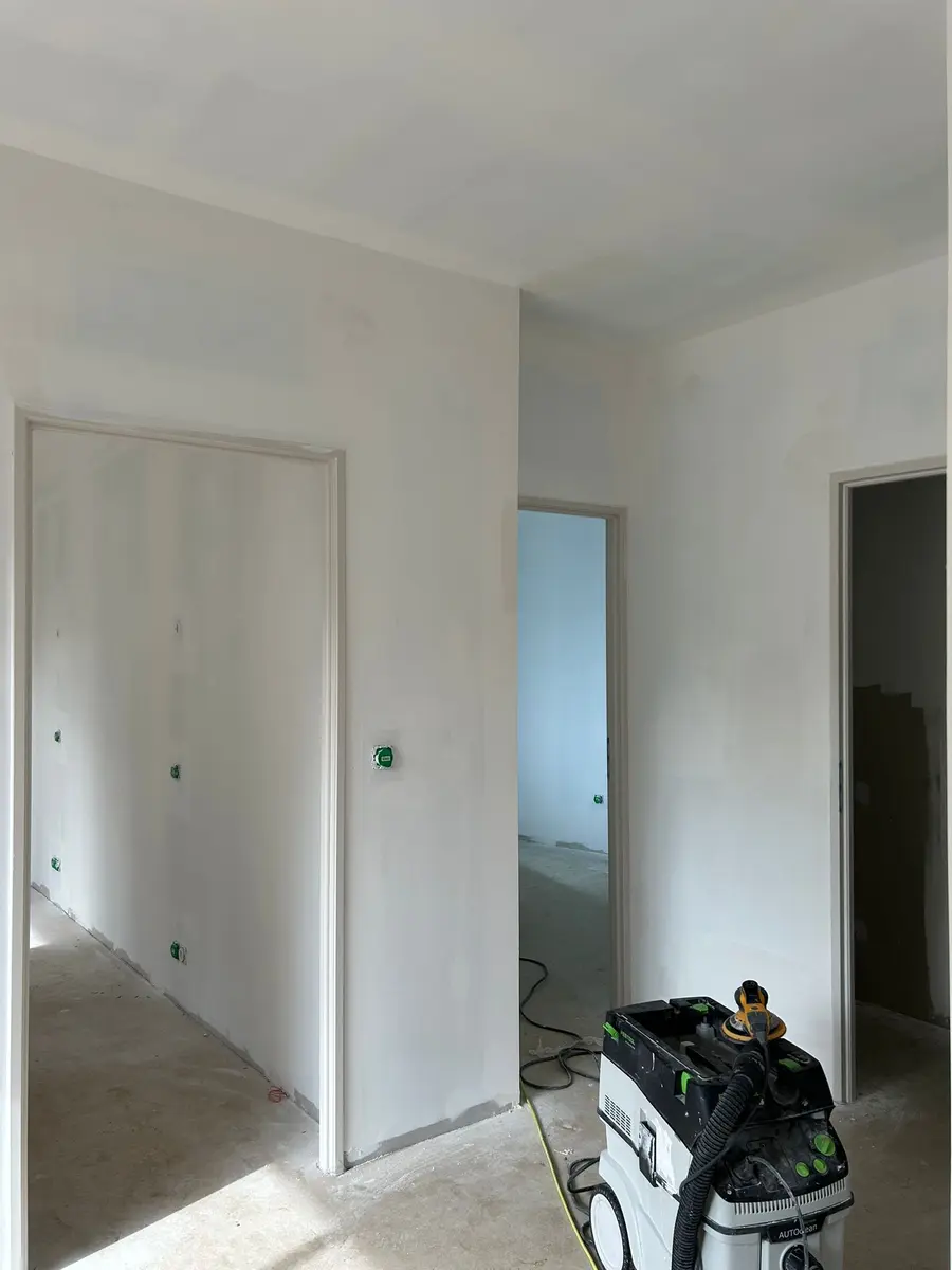 Mur en préparation avec des portes blanches et du matériel de chantier au sol.
