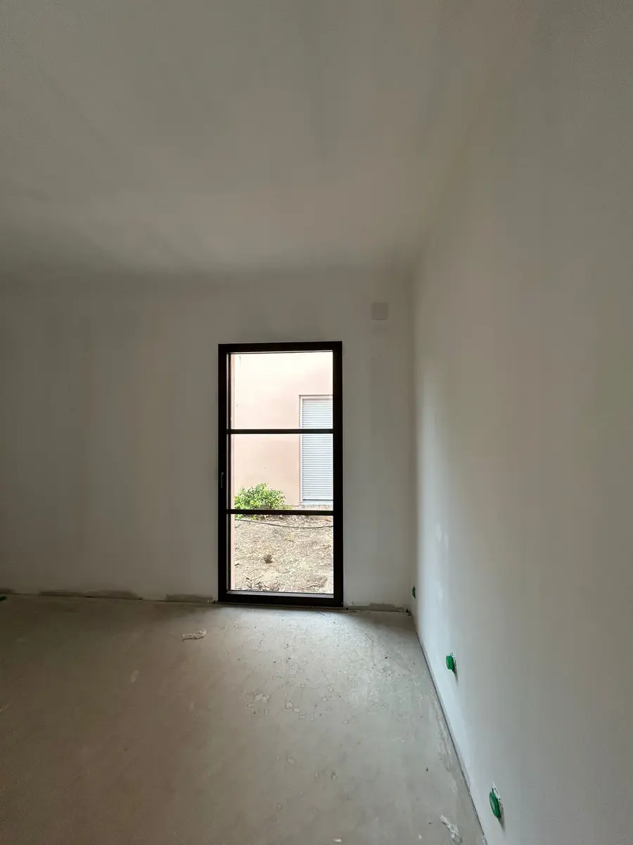 Pièce vide en travaux avec une porte vitrée noire et un sol brut.