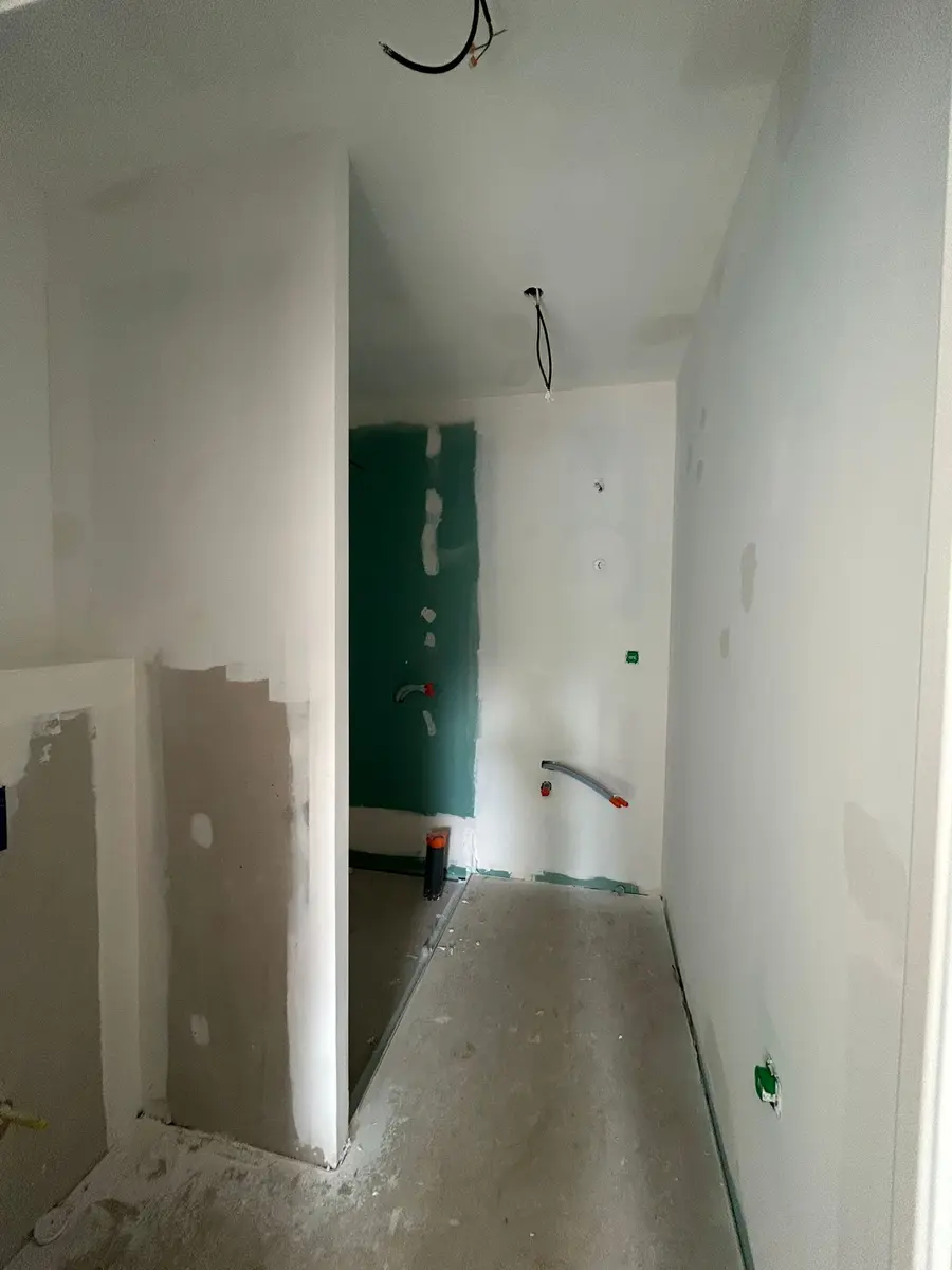 Couloir en travaux avec des câbles en attente et une plaque de plâtre verte.