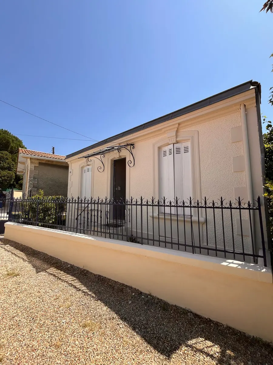 Vue latérale d’une maison à façade claire et volets fermés.