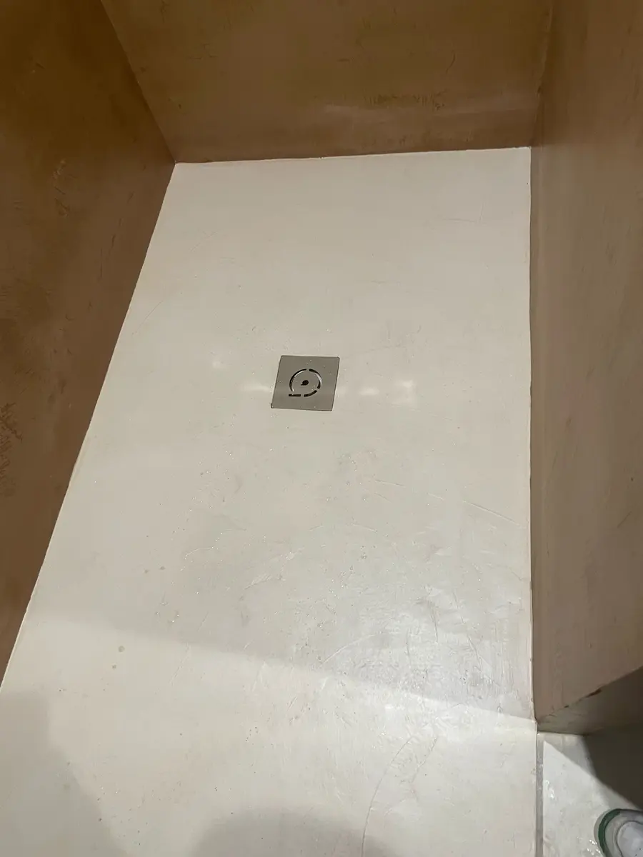 Receveur de douche clair entouré de murs beiges à effet de matière.