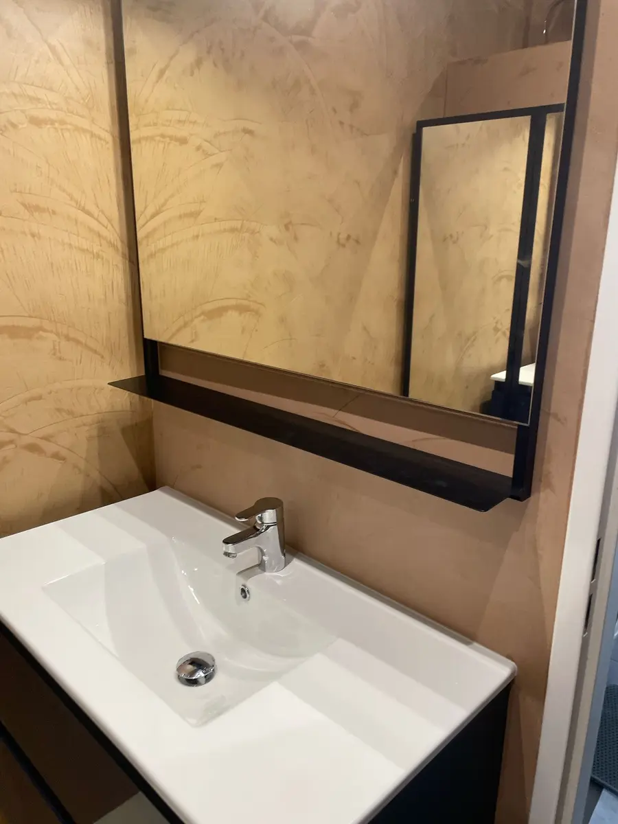 Vasque blanche et miroir noir devant un mur beige à effet minéral.