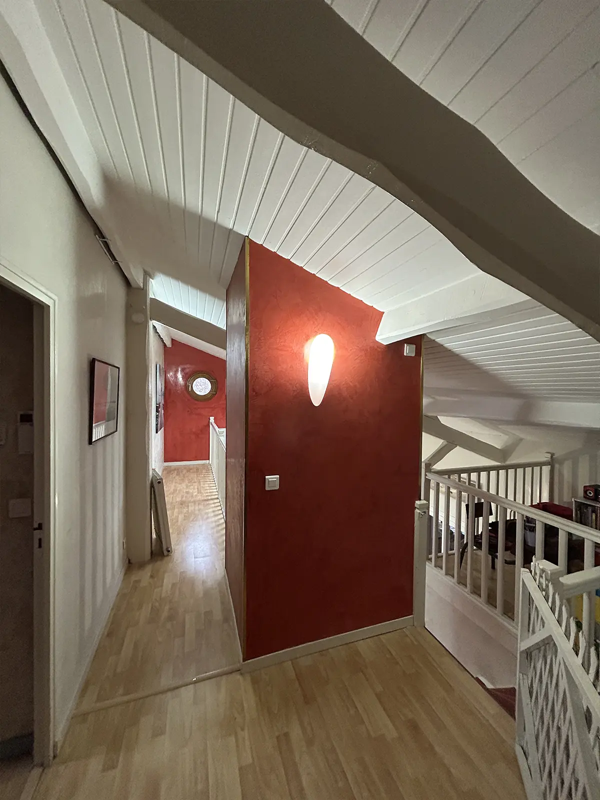 Palier à garde-corps blanc avec un mur rouge et un plafond sous pente.