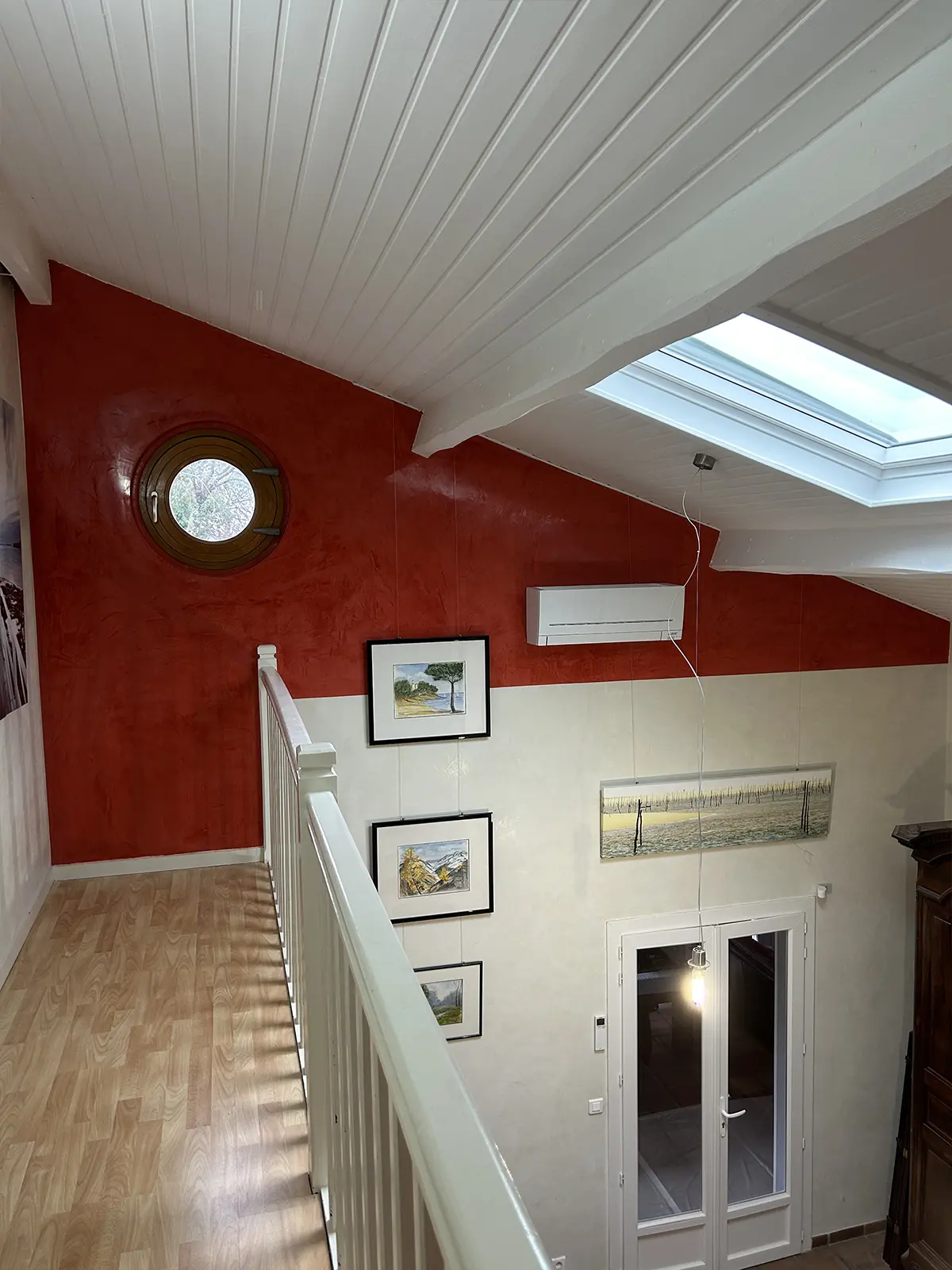 Vue d’un palier avec un mur rouge, une fenêtre ronde et une fenêtre de toit.