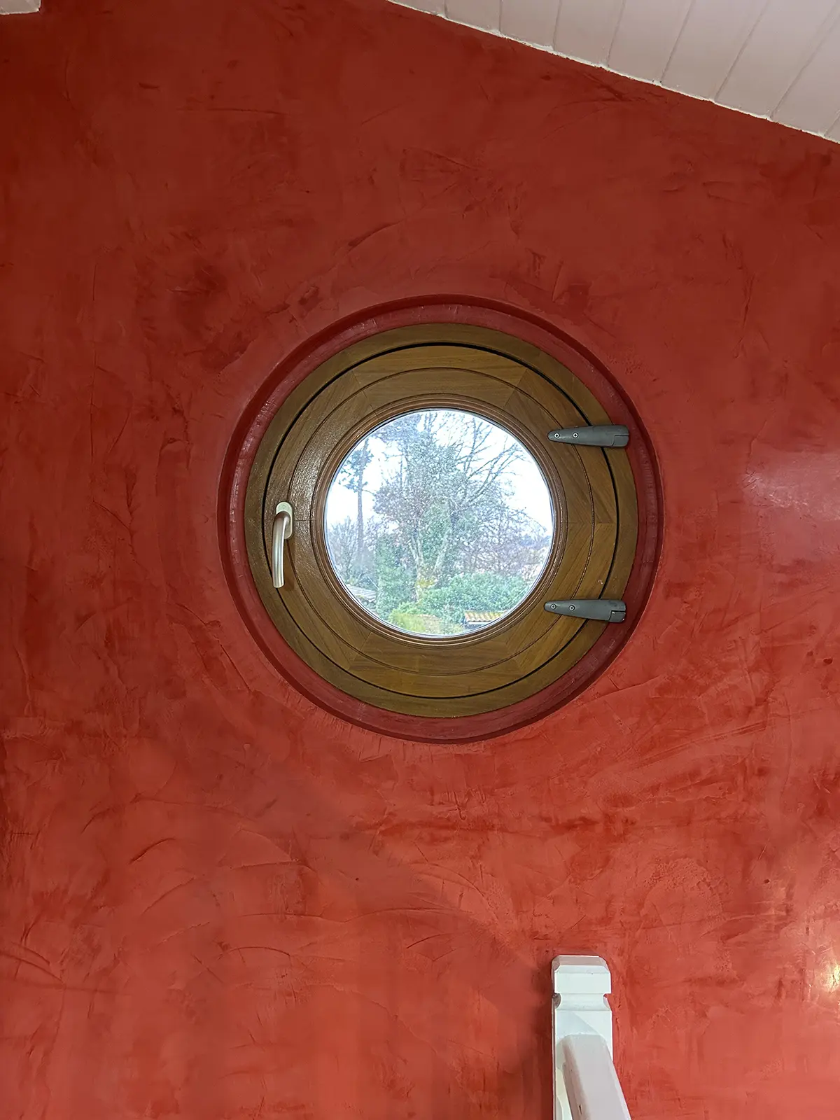 Gros plan sur une fenêtre ronde au milieu d’un mur rouge à effet de matière.