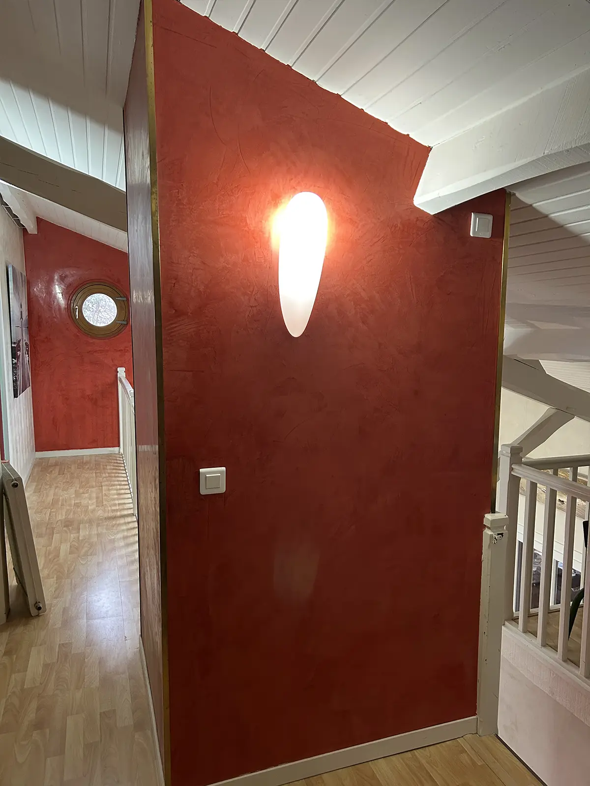 Mur rouge texturé avec une applique lumineuse et un plafond blanc.