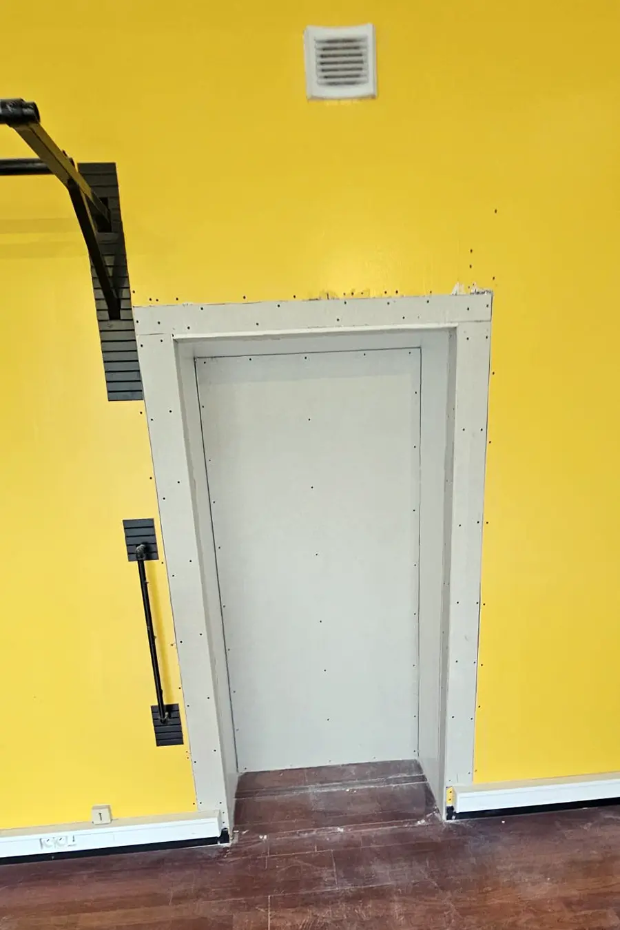 Porte blanche encadrée de protections sur un mur jaune.