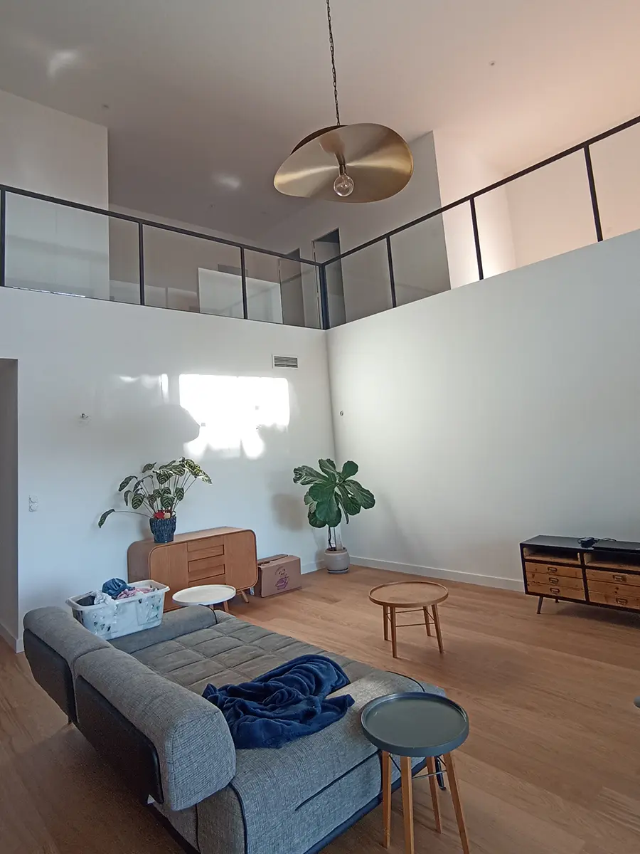 Séjour à double hauteur avec un canapé gris et un sol à effet bois.